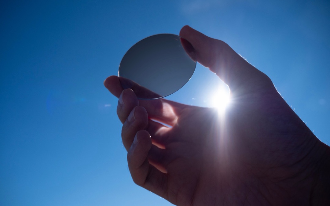 Hand hält ein selbsttönendes Brillenglas gegen die Sonne, das Glas ist im Sonnenlicht eingedunkelt